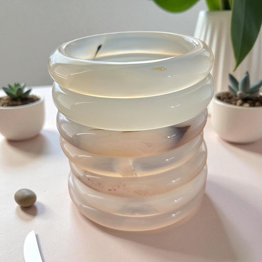 Stacked glass candle holder on a table with plants in the background