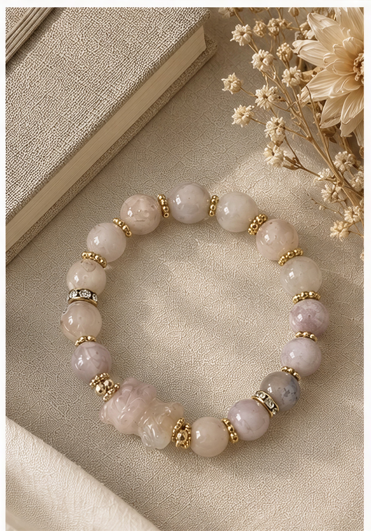 Sakura Agate carved bear bracelet with pale round beads and gold-tone spacers beside dried flowers.