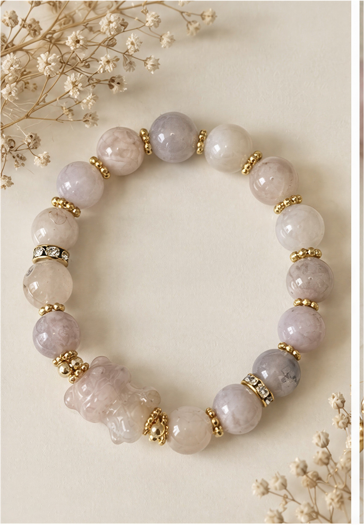 Pale Sakura Agate bear bracelet with gold-tone accents arranged beside a book and dried flowers.