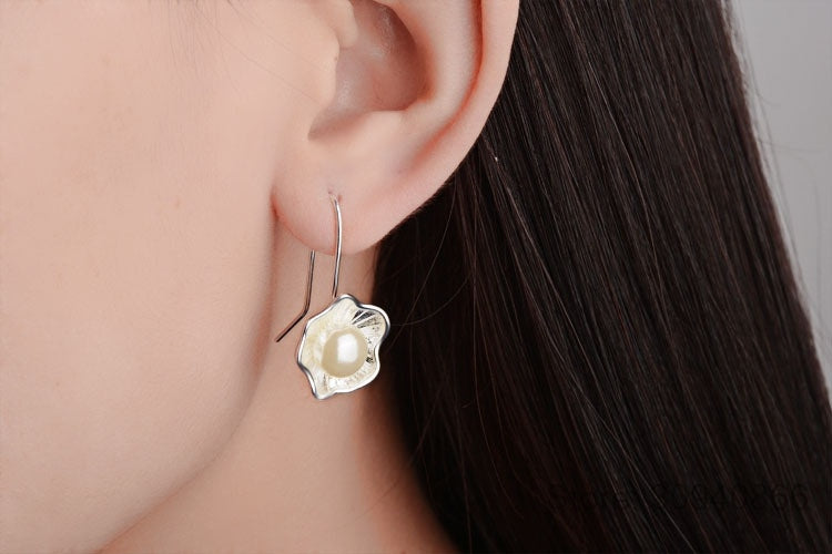 Pearl earring worn by a person with dark hair, close-up of ear.