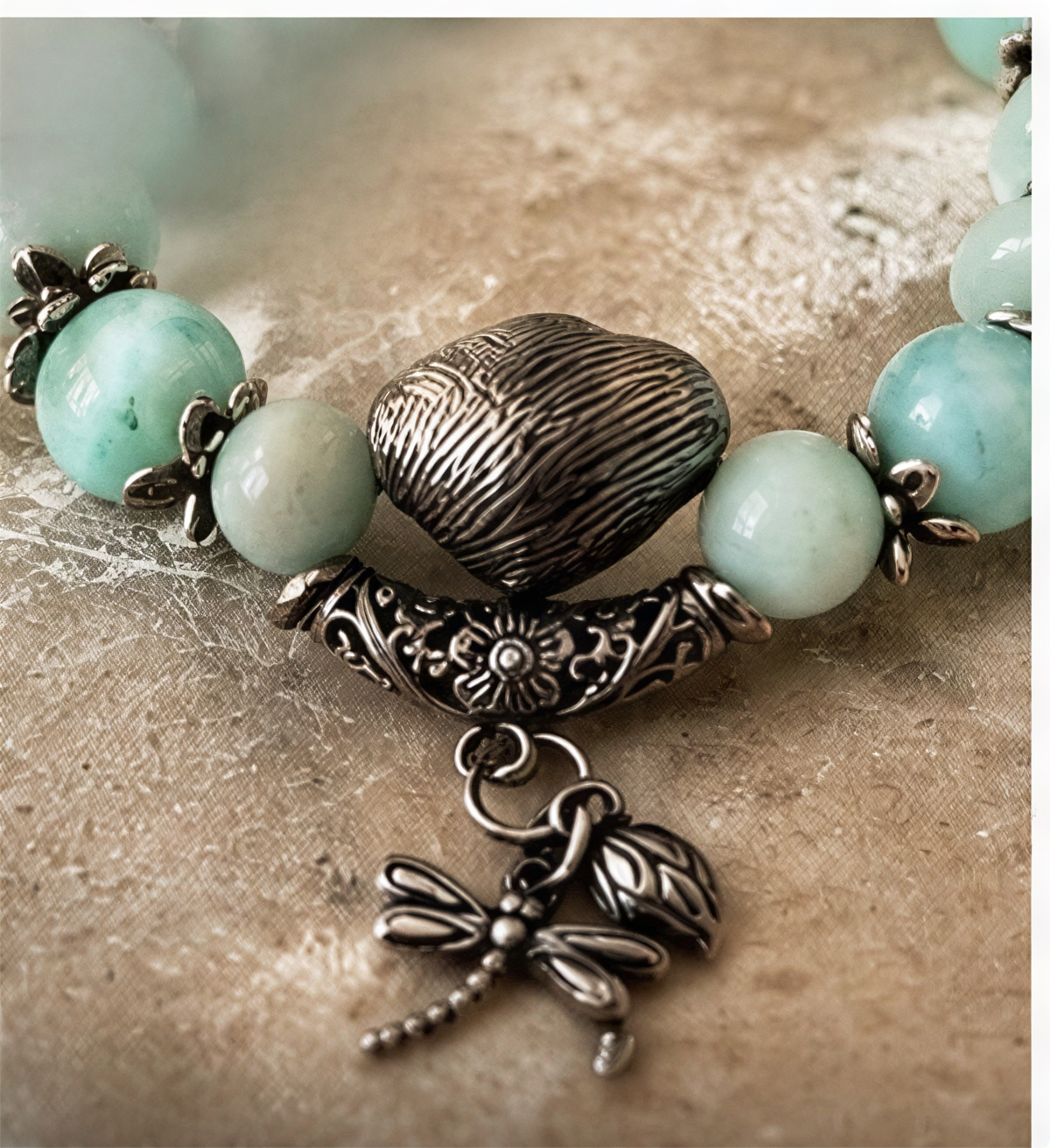 Close-up of Larimar beads, textured silver-tone centerpiece, floral accent, and dragonfly charm.