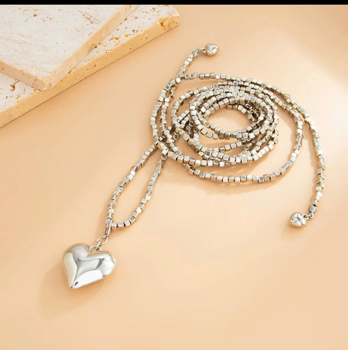 Silver beaded necklace with a heart pendant on a beige surface