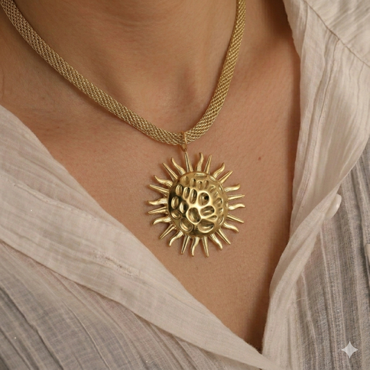 Gold sun-shaped pendant necklace on a person wearing a light-colored top.