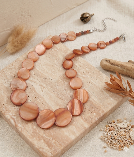Necklace with peach-colored beads on a textured surface with natural elements