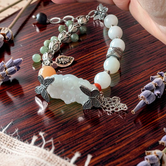 Water jade hand carved sakura flower bracelet with silver butterfly charms and orange agate on wood surface with lavender