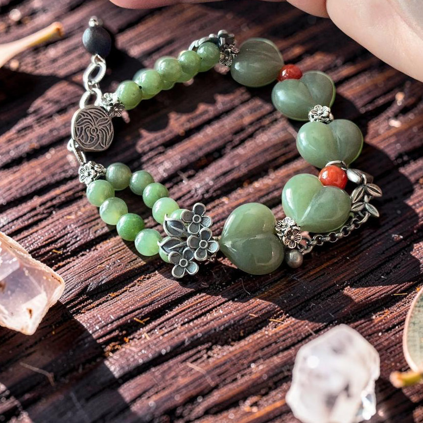 Green jade hand carved heart bracelet with silver floral charms and carnelian accents on rustic wood