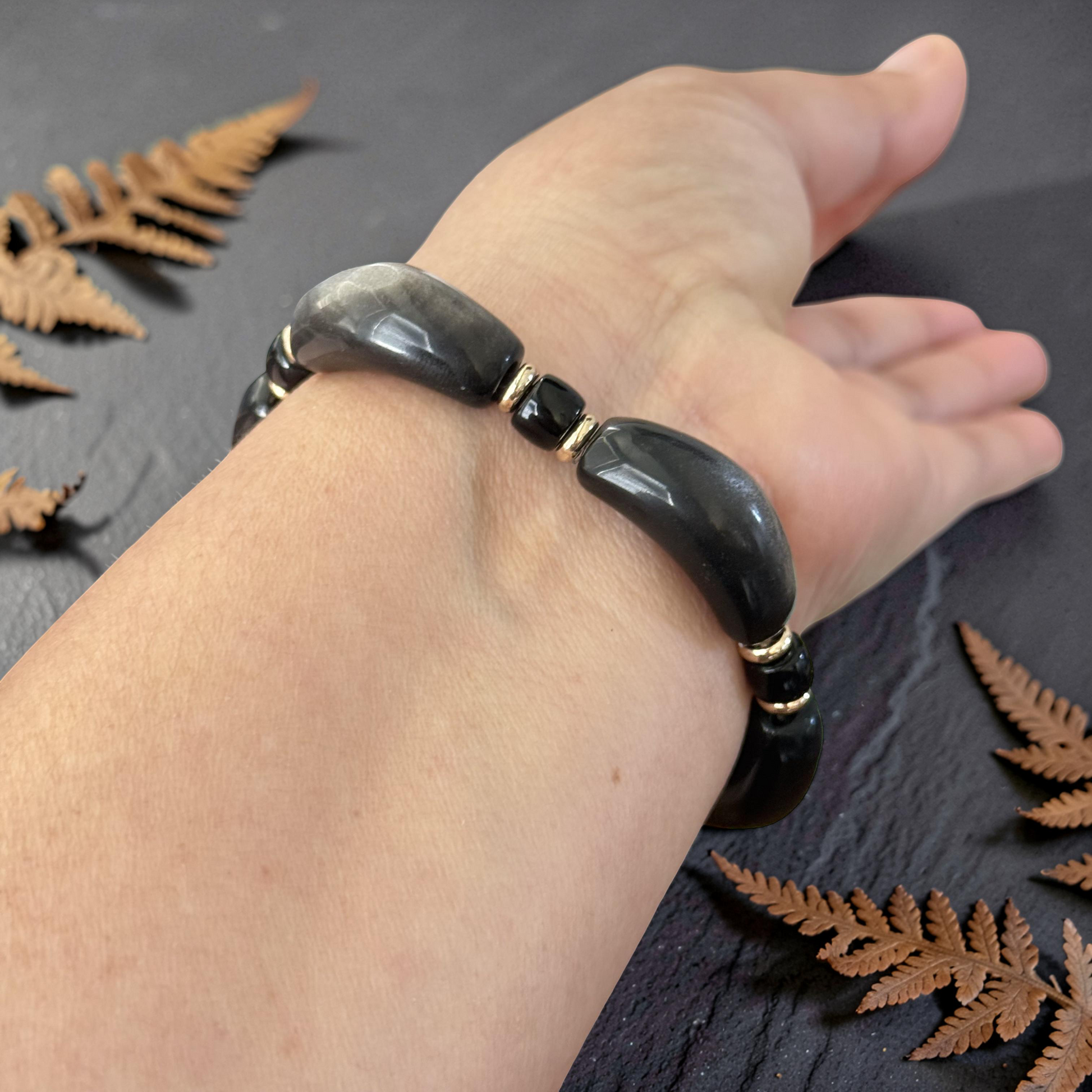Two Silver Obsidian Bracelets held in hand with greenery