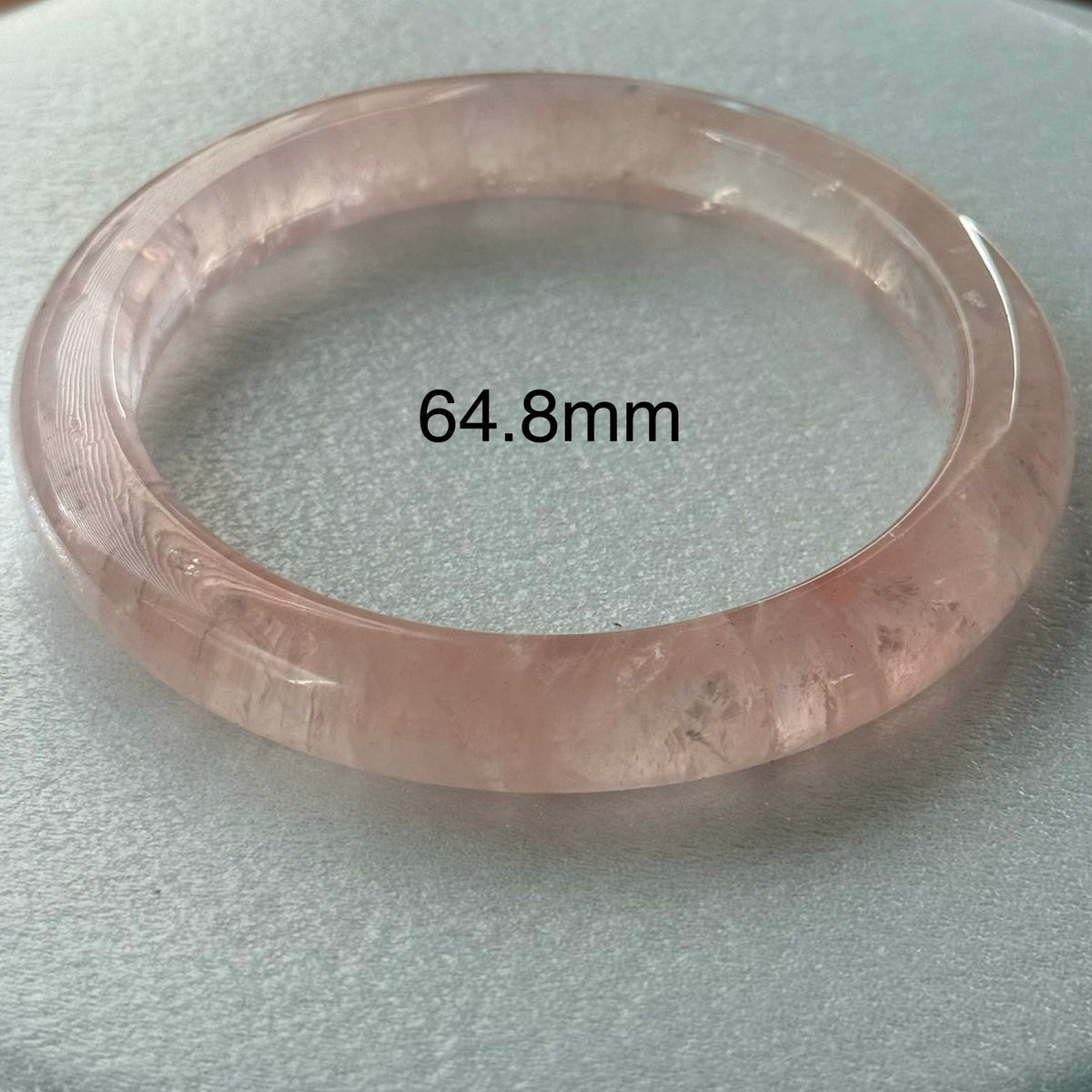 A translucent pale pink bangle bracelet displayed on a light gray textured surface, with the text '64.8mm' overlaid in the center.