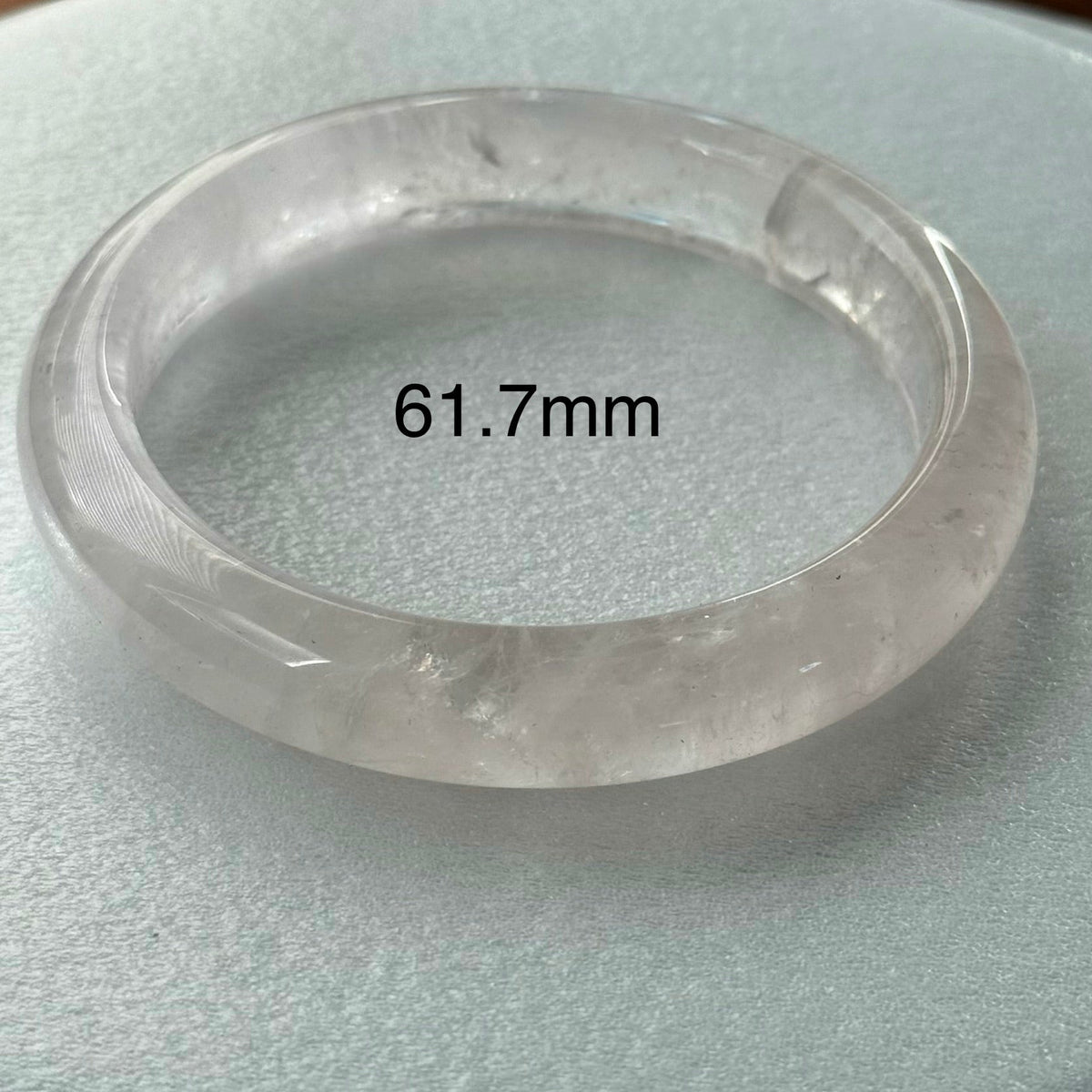 A translucent round bangle bracelet, likely made of clear quartz or glass, resting on a light gray textured surface. The text '61.