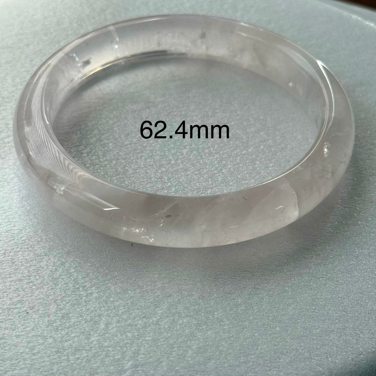 A translucent clear stone bangle bracelet displayed on a light gray textured surface, with a black text overlay reading '62.4mm'.