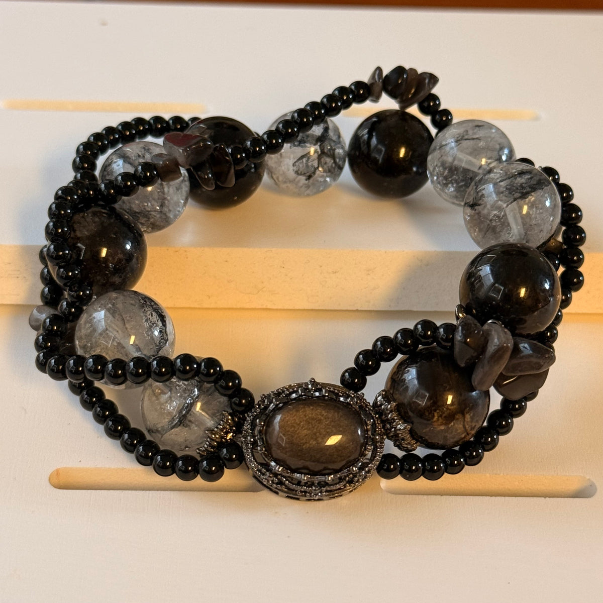 Black and clear beaded bracelet with smoky-brown chip accents and an ornate oval centerpiece on a light display.