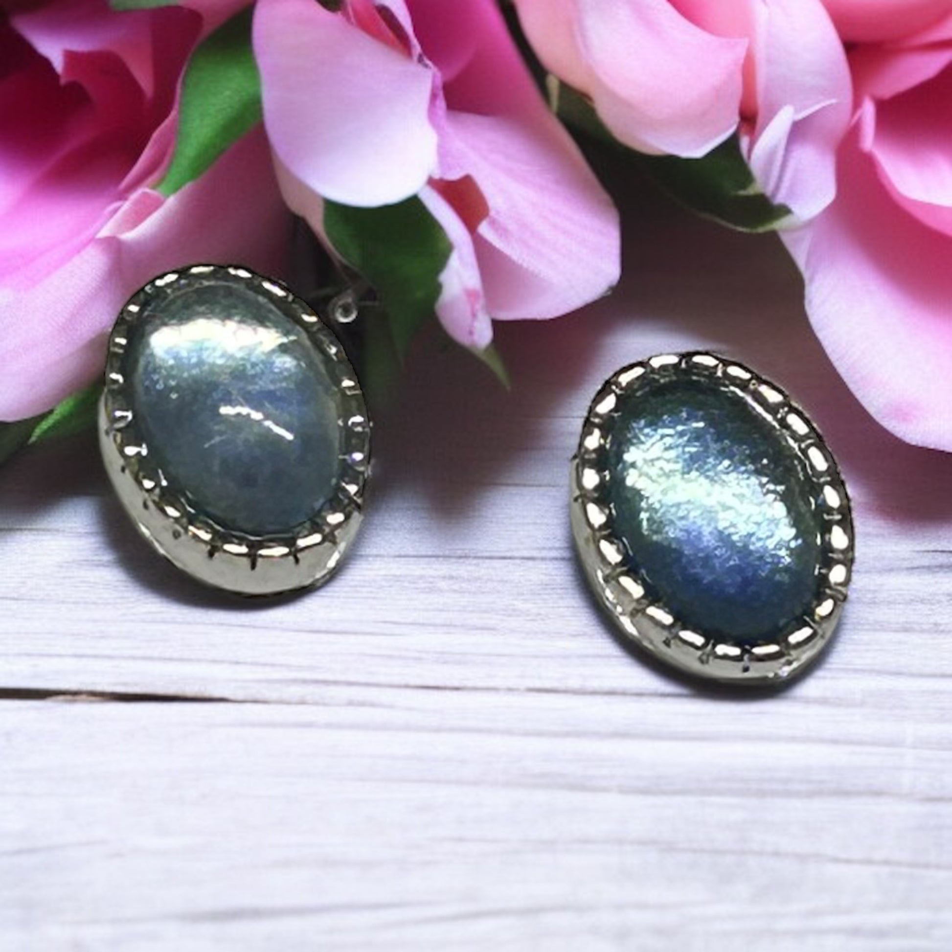 Pair of earrings with blue gemstones on a white surface with pink flowers in the background